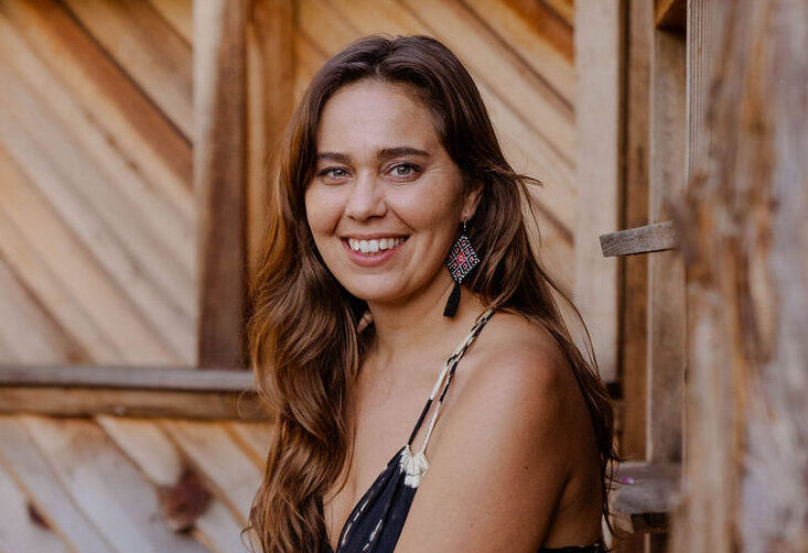 Smiling woman seated on a wooden porch with purple flowers in the foreground.